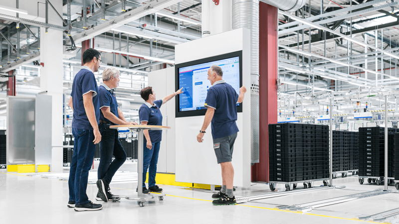 Industrial workers analyzing real-time manufacturing data on control dashboard in connected factory.