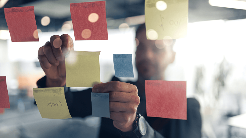 Close-up of hands placing sticky notes on board, illustrating brainstorming, project planning, and collaborative strategy development.